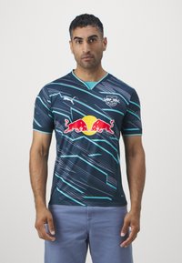 Sötétkék sportmez türkiz színű akcentussal. V-nyakú, rövid ujjú, dinamikus vonalmintázattal rendelkezik. A Red Bull logója kiemelkedően látható.