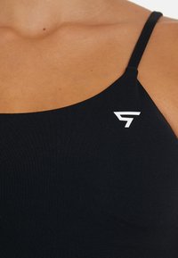 Čierna športová podprsenka s ryhľovým vzorom a tenkými ramienkami, s bielym logom na ľavej strane. Hladká textúra a priliehavý strih.