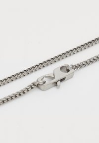 Sølvfarvet kæd necklace med et nærbillede af en rustfri stål hummerlås på en hvid baggrund.