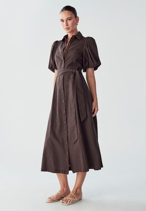 Brown linen midi dress with puff sleeves, button front, belted waist, and side slits. Worn with flat, strappy sandals.