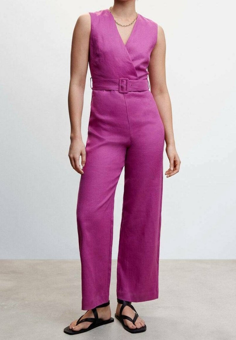 Combinaison fuchsia avec un décolleté en V à nouer, design à jambe large, taille ceinturée et tissu texturé. Associée à des tongs noires.