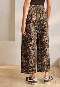 Pantalons larges en imprimé léopard dans des tons brun et noir avec une taille élastique, associés à des baskets sombres avec des accents blancs.
