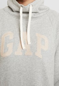 Felpa grigia con logo "GAP" rosa pallido, colletto con cordino e tessuto morbido. Presenta una vestibilità comoda e dettagli a coste sui polsini.