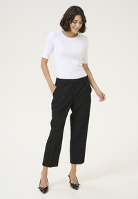 Top fitted bianco a maniche corte abbinato a pantaloni neri a vita alta e décolleté con punta a stiletto neri. Tessuto liscio, design su misura.