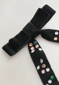 Must mustriba kahega, millel on kaks saba ja kaunistatud mitmevärviliste rhinestone'idega, mis on erinevates kujudes ning paiknevad ühel küljel.