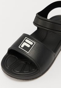 Must must sandaal, mille paksu rihmaga, millel on valge logo. Valmistatud kummist, tekstuuriga jalalaba ja kaarekujulise solega mugavuse tagamiseks.