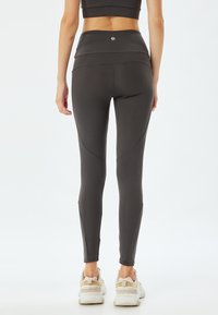 Czarne legginsy z wysokim stanem o gładkiej teksturze, z zaokrąglonymi szwami i małym logo na pasie; w połączeniu z jasnymi sneakersami.