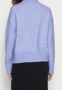 Jasnoniebieski wełniany sweter z prążkowanym kołnierzem i dołem, charakteryzujący się luźnym krojem i opadającymi ramionami. Widać również czarną spódnicę.