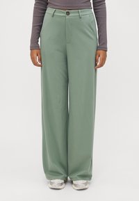 Weite Hose aus hellgrünem Stoff mit Knopfverschluss und vorderen Taschen. Glatte Textur mit lockerer Passform.