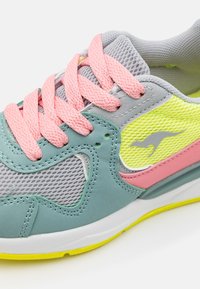 Närbild av en flerfärgad sneakers med rosa snörning, grå mesh, turkosa detaljer och en gul känguru-logga på sidopanelen.