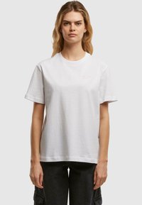 Weißes Baumwoll-T-Shirt mit kurzen Ärmeln und Rundhalsausschnitt. Mit "VERTRAUE DEINEM HERZEN" in Pink auf der Vorderseite bedruckt. Einfaches und unaufdringliches Design.