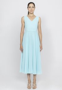 Jasnoniebieska, bezrękawnikowa sukienka z plisami i dekoltem w kształcie litery V. Materiał elegancko opada do połowy łydki, w połączeniu z beżowymi sandałami na paski.