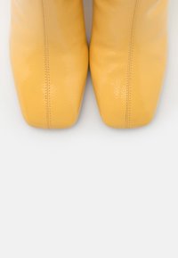 Bottines en cuir jaune avec une texture lisse, bout pointu et des détails de couture subtils le long des côtés.