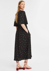 Zwarte maxi jurk met een kersenprint; korte mouwen, elastische taille en zijzakken; gedragen met rode sandalen met bandjes.