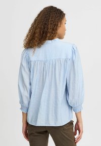 Blusa azzurro chiaro, con texture, maniche a sbuffo e dettagli a yoke. Polsini elasticizzati e orlo curvo. Adatta per un look casual.