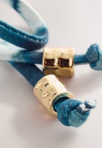 Siniste ja valgete mustriga kangast lipsud kuldsete metallikdetailidega. Disainil on sõlmitud otsad ja riistvaral sile, läikiv pind.