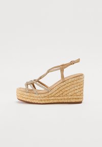 Beige kilehæle sandal med fletvævet jute sål, prydet med metalstropper og spænde til ankelrem. Tekstureret overflade og åben tå-design.