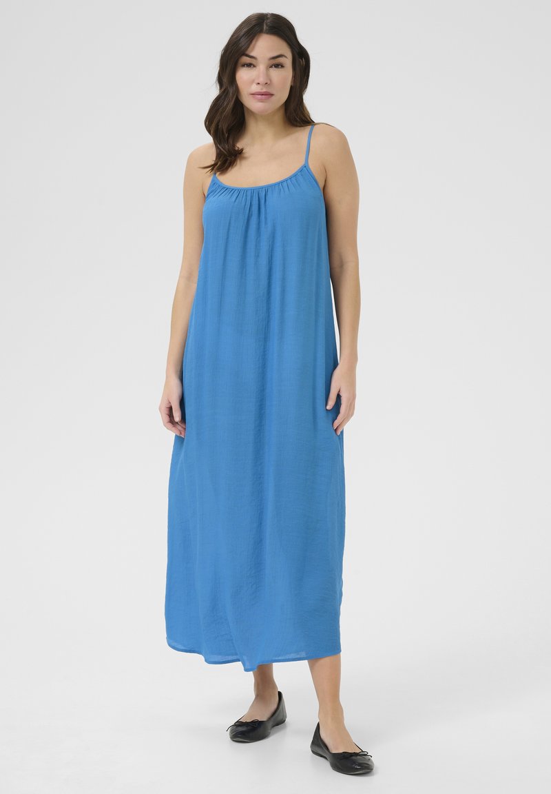 Vestido maxi sin mangas de color azul, hecho de tejido ligero. Presenta un escote fruncido y una silueta fluida, combinado con zapatos planos negros.