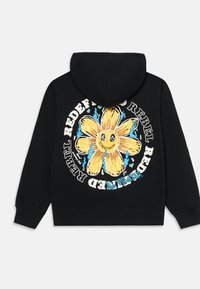 Sort hættetrøje med et stort gult blomstergrafik omgivet af blå flammer og hvid tekst, der står "Rebel Redefined" på ryggen.