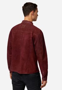 Burgundy mockaskjacka med långa ärmar, ryggparti med detalj och en läderetikett vid kragen. Har en lätt texturerad yta.