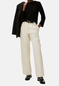 Czarny dziergany sweter, kremowe spodnie o szerokich nogawkach, czarny pasek ze złotą klamrą oraz czarne mokasyny z detalem klamry. Dopasowany żakiet zarzucony na ramię.