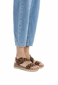 Sandali con stampa leopardata, cinturini in velcro, suola in tono chiaro, e design open-toe, abbinati a pantaloni in denim blu a vita corta.