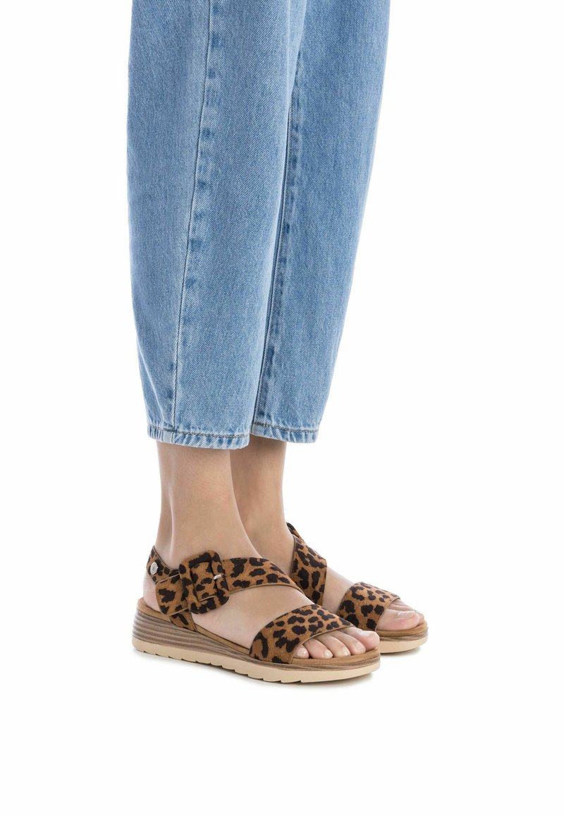 Sandali con stampa leopardata, cinturini in velcro, suola in tono chiaro, e design open-toe, abbinati a pantaloni in denim blu a vita corta.