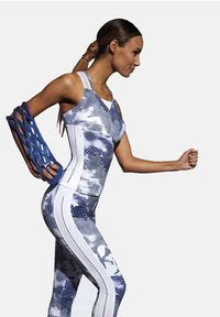 Niebieska i biała sportowa koszulka bez rękawów z wzorem w plastry miodu, w połączeniu z dopasowanymi legginsami i niebieskim teksturowanym akcesorium na ramię.
