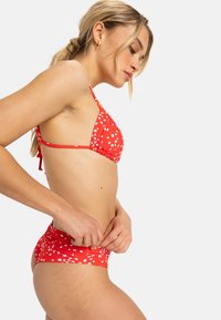 Rode bikini met wit bloemenpatroon; heeft een driehoek-top met verstelbare bandjes en een bijpassende high-waisted broek.