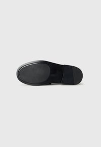 Schwarze Schuhsohle mit glatter und gerippter Textur, leicht geschwungener Form und festem Material. Inklusive Branding und ohne sichtbare Akzente.