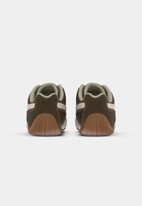 Zapatillas Puma marrones y beige vistas desde atrás, destacando las suelas de goma y el logo en las pestañas del talón.