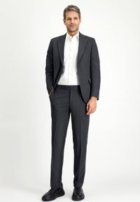 Completo grigio scuro con giacca aderente e pantaloni abbinati, abbinato a una camicia bianca con bottoni e sneakers nere. Tessuto morbido, design su misura.