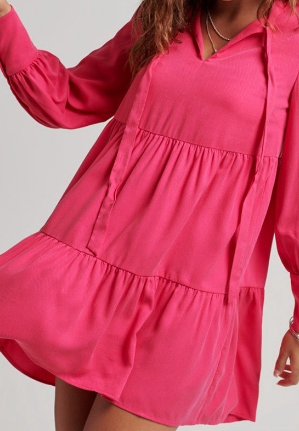 Robe longue rose à manches longues avec un col en V, un ourlet à volants superposés et un tissu léger. Caractérisée par une coupe ample et une texture subtile.
