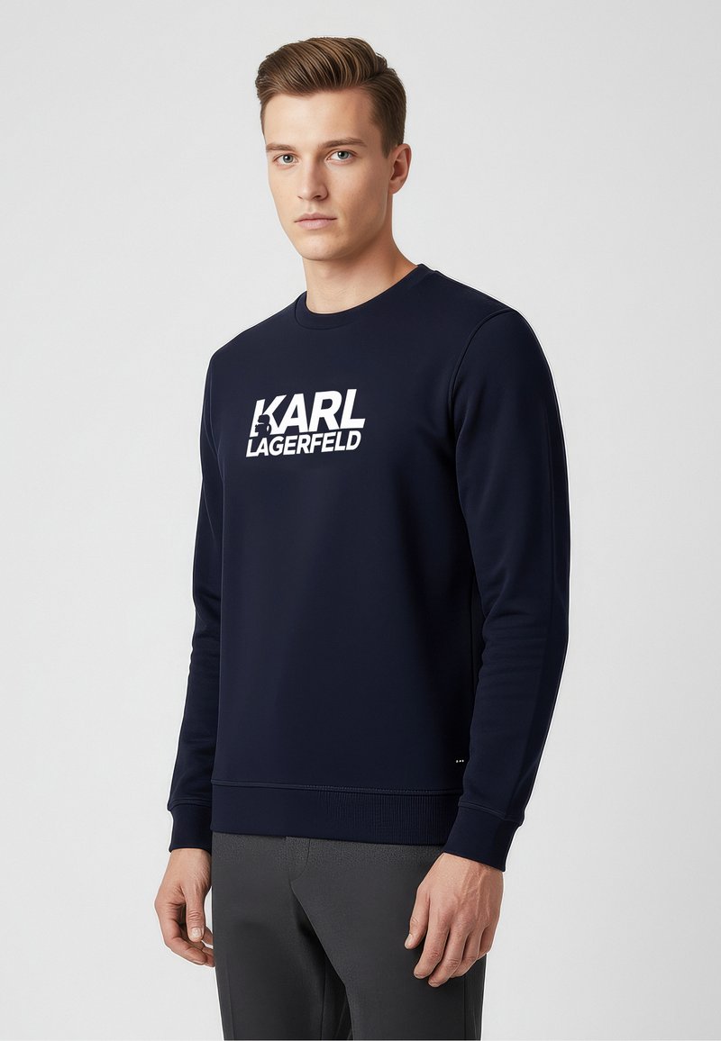 Marineblaues Sweatshirt mit rundem Halsausschnitt und langen Ärmeln, das ein auffälliges weißes "KARL LAGERFELD"-Logo auf der Vorderseite trägt. Glatte Textur.