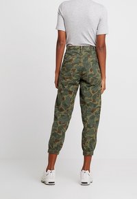 Groene camouflage joggers van katoen met elastische boorden, in een relaxte pasvorm en met achterzakken, gecombineerd met een grijs t-shirt en witte sneakers.