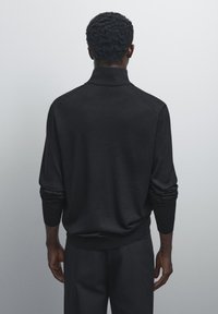 Black knit sweater featuring a high collar, long sleeves, and a relaxed fit, paired with matching dark pants. Soft texture and minimal design.