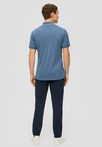 Męska krótki rękaw polo w jasnoniebieskim kolorze, wykonana z miękkiego materiału, w połączeniu z ciemnogranatowymi spodniami i białymi butami. Minimalistyczny design.