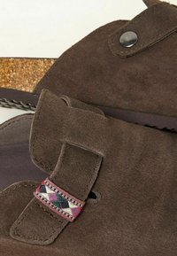 Brown suede sandals feature an adjustable strap with a geometric patterned accent and a cork footbed. Textured sole provides grip.