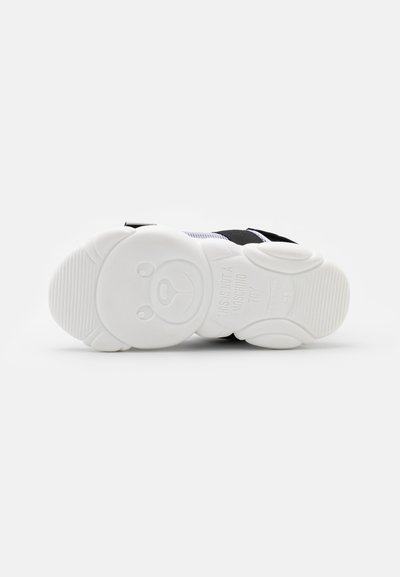 Shoe atléticas pretas com uma sola de borracha branca com um design de rosto de urso. Padrão de aderência texturizado na sola e faixa de fecho segura.