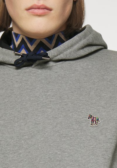 Hanorac gri cu un șnur, având o broderie mică de zebră multicoloră. Sub aceasta, o guler cu un model în nuanțe de albastru și maro.