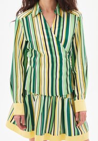 Ensemble blouse à rayures et jupe en vert, jaune et blanc. Caractérisé par un design portefeuille, des manches longues et des accents jaunes aux poignets et à l'ourlet.