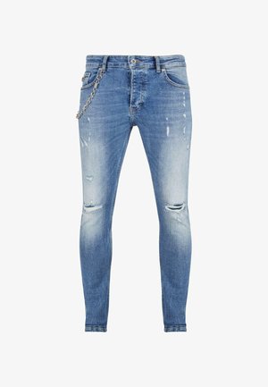 Kitsad sinised teksad, millel on pleekinud pesu, sisaldavad kahjustatud kohti ja põlvekilu. Vööl on hõbedane ketidetail.