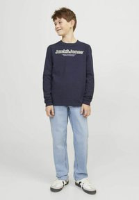 Tamnoplava majica dugih rukava s bijelim logotipom "Jack & Jones", u kombinaciji s svijetloplavim trapericama i crno-bijelim tenisicama. Jednostavan dizajn i opušteni kroj.