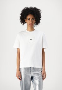 Weißes Baumwoll-T-Shirt mit einem quadratischen strukturierten Einsatz mit Perforationen und einem schwarzen Logo in der Mitte. Kurzärmelig, lockere Passform.