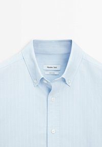 Light blue button-up shirt with vertical stripes, made of soft fabric. Features a classic collar and white button fastenings. Brand label visible.