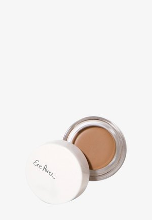 Creamy concealer in a clear jar with a white lid. The product is a warm, medium beige shade with a smooth texture.