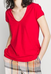 T-shirt rosso a maniche corte con scollo a V e vestibilità comoda, abbinato a pantaloni a quadri con accenti arancioni e blu. Tessuto morbido e leggero.
