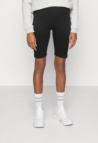 Czarne szorty rowerowe wykonane z elastycznego materiału, sięgające nad kolano. Połączone z białymi sneakersami i paskowanymi białymi skarpetami.