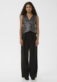 Csillogó fekete ujjatlan felső flitterekkel és V-nyakkivágással, magasan derekú fekete bő szárú nadrággal. Sima textúra.