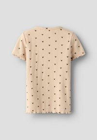 Jasno-beżowa koszulka z prążkowanego materiału, zdobiona rozsianym wzorem motyli w ciemnym brązie. Krótkie rękawy i falbaniasty dół dopełniają całość.